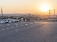 the sun sets behind a road that stretches into a rural valley with lots of buildings in the background