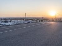 the sun sets behind a road that stretches into a rural valley with lots of buildings in the background