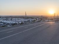 the sun sets behind a road that stretches into a rural valley with lots of buildings in the background