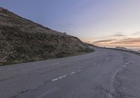 an empty empty road at sunset with traffic going by on the side of it near a cliff