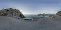 a panoramic view of a road on the shore at sunset near water and some rocks