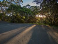 the sun is setting behind a road and trees in the distance in a park at sunset