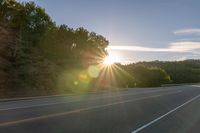 a car that is parked on the side of a road at sunset in a highway with the sun breaking through the trees