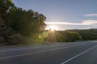 a car that is parked on the side of a road at sunset in a highway with the sun breaking through the trees