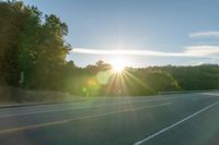 a car that is parked on the side of a road at sunset in a highway with the sun breaking through the trees