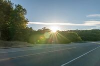 a car that is parked on the side of a road at sunset in a highway with the sun breaking through the trees