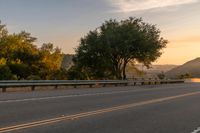 a truck is driving down the highway at sunset with trees on both sides of road