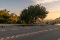 a truck is driving down the highway at sunset with trees on both sides of road