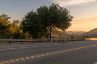 a truck is driving down the highway at sunset with trees on both sides of road