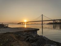 a photo of the sun setting over a large body of water with a bridge in the distance