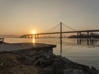 a photo of the sun setting over a large body of water with a bridge in the distance