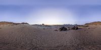 the sun is setting over sand dunes in the desert and a group of rocks are on top