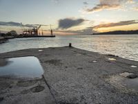 sunset at the sea and a large ship in the water under clouds, near a concrete dock and cement wall