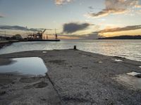 sunset at the sea and a large ship in the water under clouds, near a concrete dock and cement wall