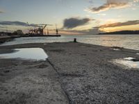 sunset at the sea and a large ship in the water under clouds, near a concrete dock and cement wall