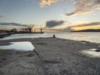 sunset at the sea and a large ship in the water under clouds, near a concrete dock and cement wall