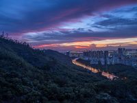 sunset on a valley below city buildings and a mountain top, with a river running through it