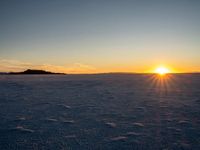 a snow boarder flying a kite into the sky at sunset on an ocean plain