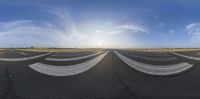 a wide angle view of an airport runway with the sun setting behind it and people standing on the tarmac