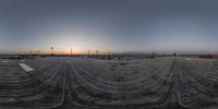 a panoramic picture of the sun setting behind a concrete parking lot and trees