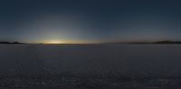 an image of the sun setting over a flat land with no clouds in sight while a mountain rises above the horizon