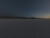 a vast desert landscape at sunset with mountains in the background that is very dark and a dark cloud is also visible