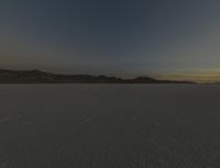 a vast desert landscape at sunset with mountains in the background that is very dark and a dark cloud is also visible