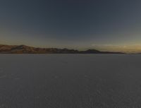 a vast desert landscape at sunset with mountains in the background that is very dark and a dark cloud is also visible