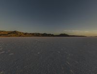 a vast desert landscape at sunset with mountains in the background that is very dark and a dark cloud is also visible