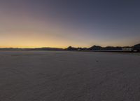 a sunset in the background with mountains and the sun setting behind it with snow covering ground