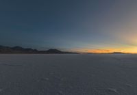 someone walks across an icy field at sunset in the distance, mountains in the distance