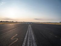 the sun is setting on a runway with a dotted path going to the left, at an airport