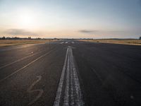 the sun is setting on a runway with a dotted path going to the left, at an airport