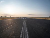 the sun is setting on a runway with a dotted path going to the left, at an airport