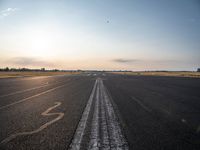 the sun is setting on a runway with a dotted path going to the left, at an airport