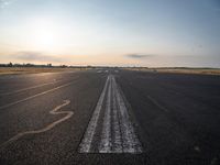 the sun is setting on a runway with a dotted path going to the left, at an airport