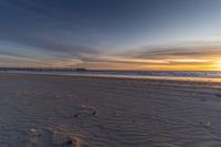 a view of the beach with footprints and the pier at sunset's end with the ocean