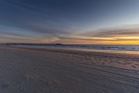 a view of the beach with footprints and the pier at sunset's end with the ocean