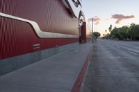 a street with a red building near it and a sunset behind it, near the curb of an empty road