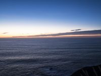 a view of the ocean at sunset from a rocky ledge overlooking the ocean with tall grass on top