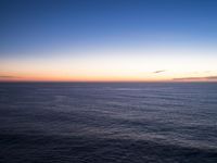 a view of the ocean at sunset from a rocky ledge overlooking the ocean with tall grass on top