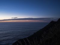 a view of the ocean at sunset from a rocky ledge overlooking the ocean with tall grass on top