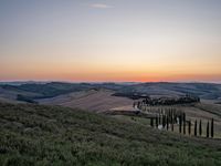 a sunset view shows the rolling hills in italy at dusk with cypress trees and grass