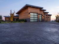 a large wooden home with driveway leading up to the garage entrance at sunset with blue skies