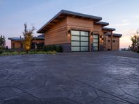 a large wooden home with driveway leading up to the garage entrance at sunset with blue skies