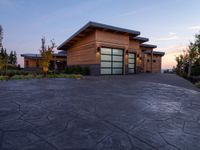 a large wooden home with driveway leading up to the garage entrance at sunset with blue skies