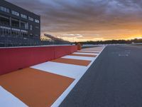 a orange and white stripe is on the ground at sunset behind the fence, a grey building stands behind it and a red wall