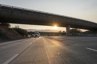 a sunset on the highway and freeway with cars driving underneath a bridge with a ramp over it