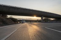 a sunset on the highway and freeway with cars driving underneath a bridge with a ramp over it