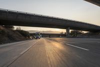 a sunset on the highway and freeway with cars driving underneath a bridge with a ramp over it